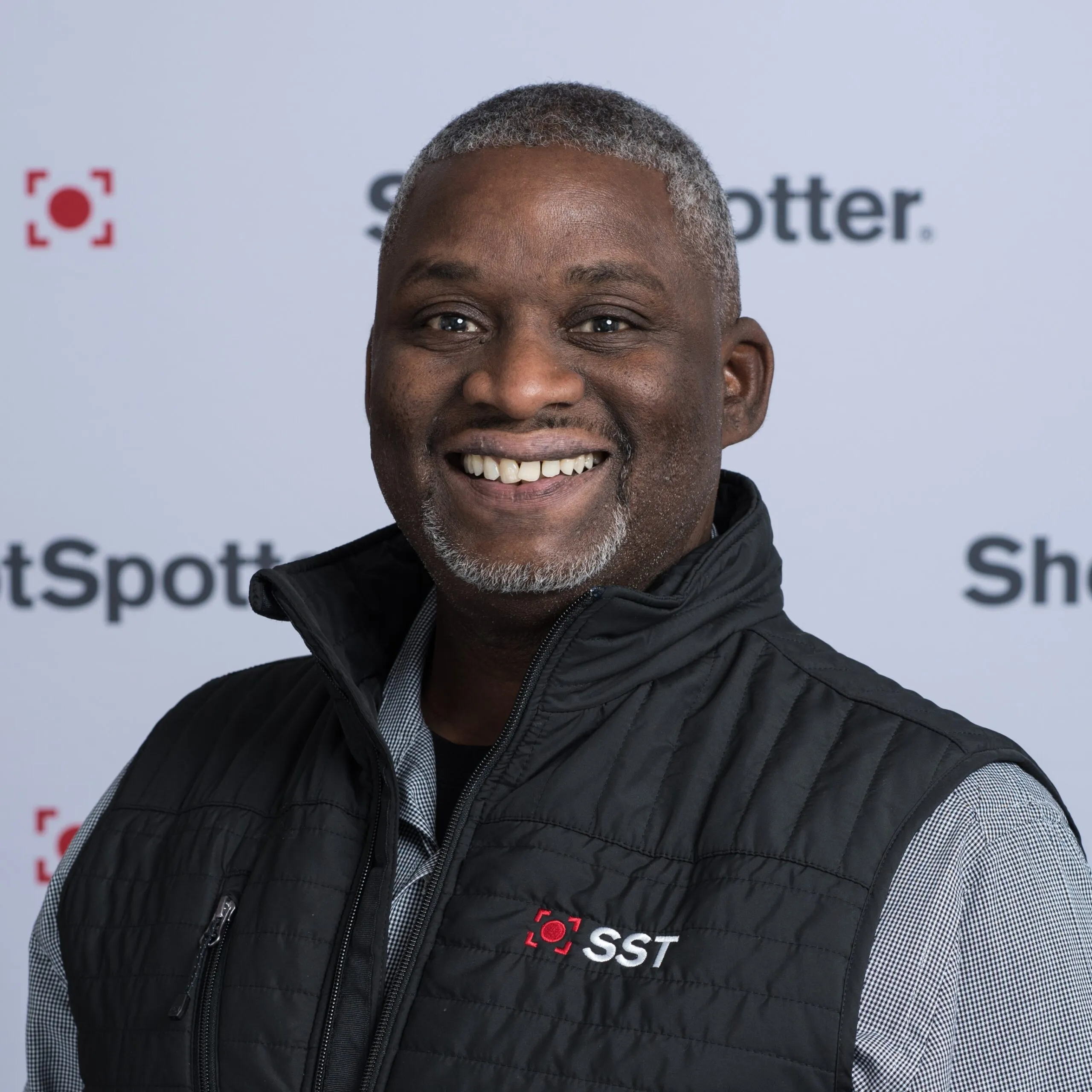 a man in a black vest smiling at the camera