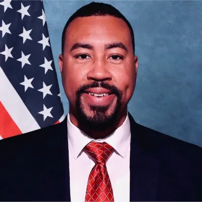 a man in a suit and tie standing in front of an american flag